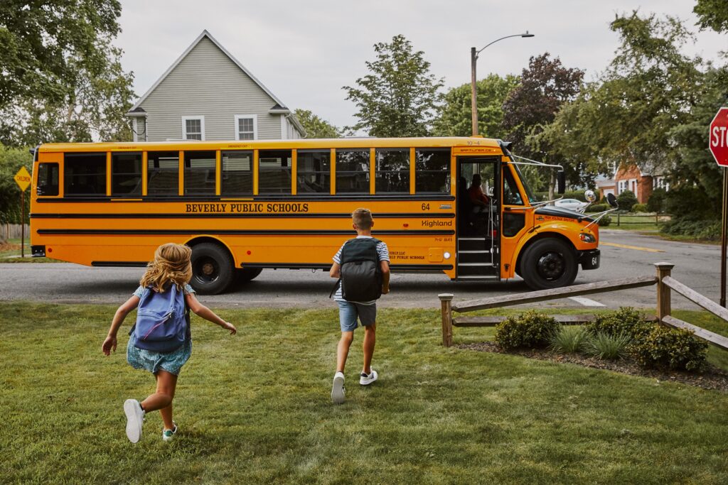 Two children running toward a school bus.